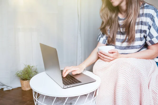 Ev kadını ve uzaktan öğrenim online eğitim. Mutlu kırpılmış güzel bayan defter başında çalışıyor kanepede battaniyeyle oturuyor ve evde kahve içiyor. Bilgisayar ve çevrimiçi dükkanlar kullanarak. — Stok fotoğraf