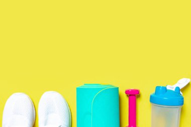 Spor ve spor malzemeleri, pembe halterler, spor ayakkabıları, su karıştırıcı şişesi ve sarı arka planda naneli yoga minderi. Kopyalama alanı olan üst görünüm. Sağlıklı yaşam tarzı.