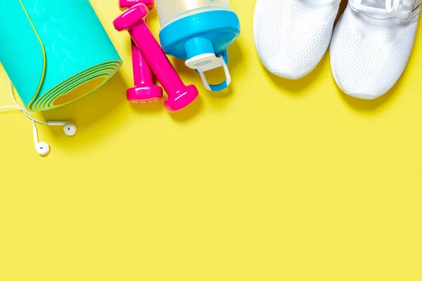 Flat Lay Sport- und Fitnessgeräte, Kopfhörer, rosa Kurzhanteln, weiße Turnschuhe, Wassermixer-Flasche und Mint-Yogamatte auf gelbem Hintergrund. Draufsicht mit Kopierraum. Gesunder Lebensstil. — Stockfoto
