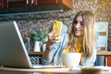 Çevrimiçi eğitim ve çalışma mesafesi. İş kadını görüntülü görüşme yapıyor. Ev ofisinden çalışan ve kahve içen mutlu ve gülümseyen bir kız. Bilgisayar ve cep telefonu kullanılıyor