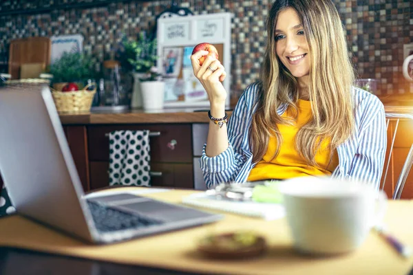 Distance learning online education and work. Woman with apple having a video call. Happy and smiling girl working from kithcen home office. Using computer and watch movies and online shops