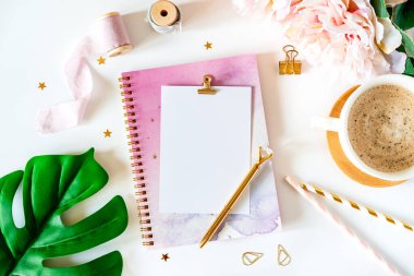 Masaüstü modeli, el yapımı DIY araçları. Beyaz çalışma masasının arka planında bir fincan kahveyle yatıyordu. Üst manzara yaprakları, kasetler, şakayıklar, altın kağıt ataçları, boş tebrik kartı, defter ve kalem..