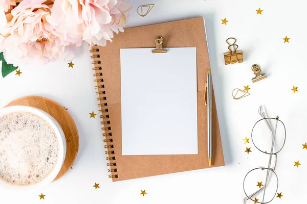 Desktop mock up scene. Flat lay of white working table background with cup of coffee putting on it. Top view glasses, flower, golden paper binder clips, blank greeting card, craft Notebook and pen.