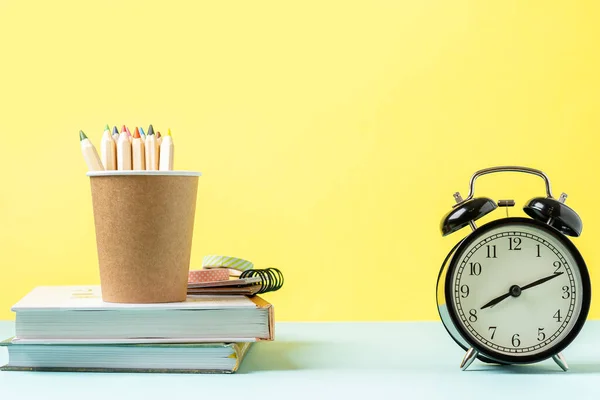 Back to school banner with black alarm clock, books and pencil. School supplies, other elements in yellow mint empty background with copy space.