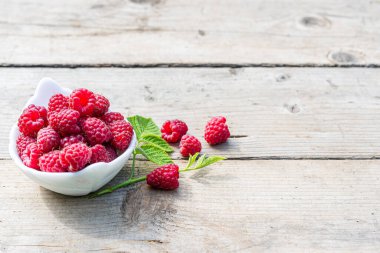Taze olgun çiftlik ahududu hasadı. Masada yapraklar, tahta arka planda beyaz tabakta..