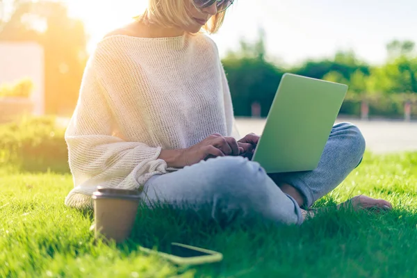 Yetişkin bir kadının bilgisayarına mesaj atması, dışarıda çimlerin üzerinde oturması. Çalışıyor ve kahve içiyor. Laptop ve cep telefonu kullanıyor. Uzaklık öğrenme çevrimiçi eğitim ve çalışma — Stok fotoğraf