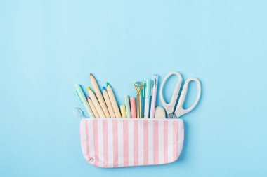 Modern, parlak, mavi ofis masaüstü, boş alanda, kalem kutusundaki yazı için okul malzemeleriyle dolu bir masa. Pembe makas, kalem ve kalemle okula dönüş konsepti