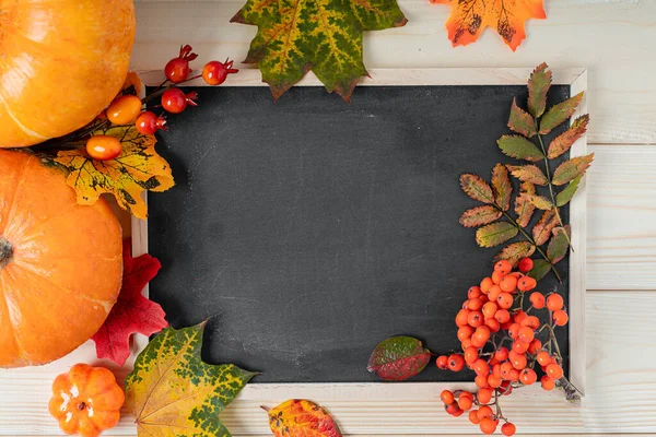 Pumpkins, berries and fallen leaves with chalk mock up blackboard frame on wooden background. Copy space for text. Halloween, Thanksgiving day or seasonal autumnal. Flat lay, top view Design.