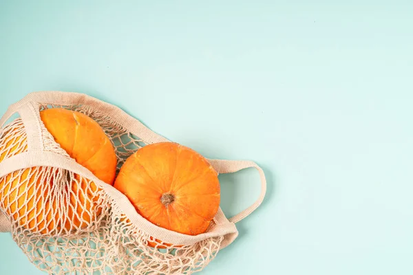 Pumpkins in string shopping bag on wooden background. Copy space for text. Halloween, Thanksgiving day or seasonal autumnal. Design mock up background. Flat lay, top view. Zero waste ecology concept.