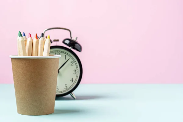 Volver a la pancarta de la escuela con despertador negro y lápiz en soporte de taza de café. Material escolar, otros elementos en color rosa menta fondo vacío con espacio de copia — Foto de Stock