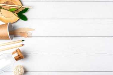 Cam kavanoz, yeşil yapraklar, defter ve geri dönüşümlü masa örtüsü manzarası. Sıfır atık, çevre dostu, doğal organik plastik konsept. Çatal bıçak takımı, toprak, beyaz ahşap üzerinde fotokopi alanı ile ayrıştırılabilir.