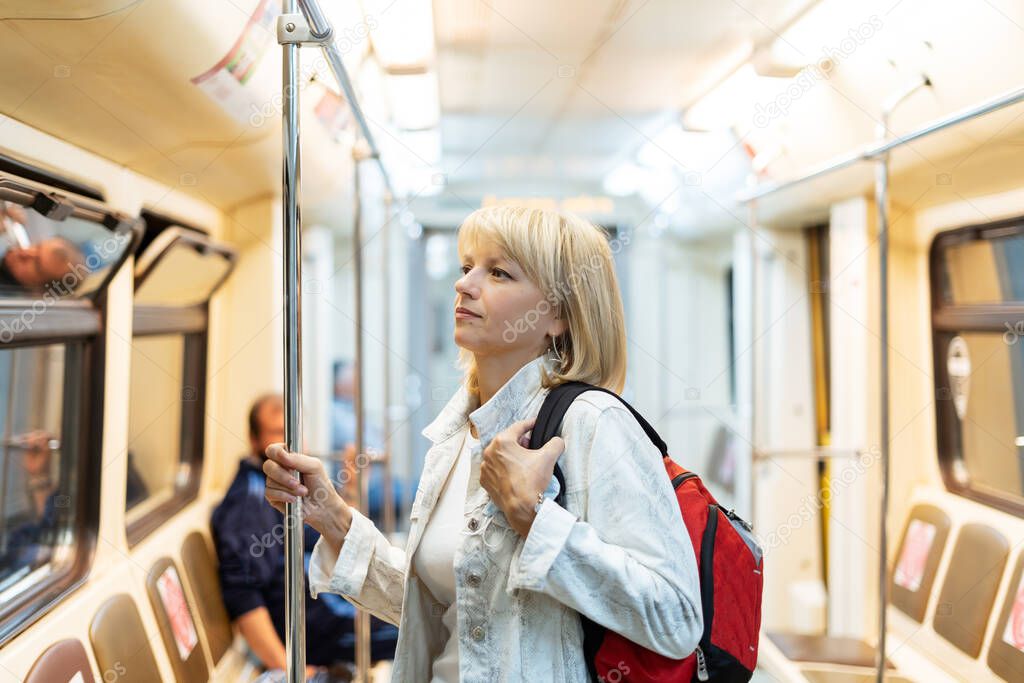 Portrait of beautiful adult woman with backpack stands in the subway and looks ahead.