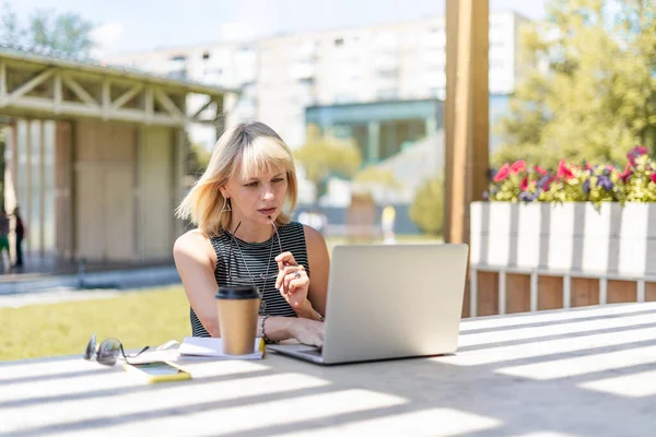 Vuxen kvinna i glasögon med videosamtal med bärbar dator utanför i parken. Glad och leende senior arbetar och dricker kaffe. Använda dator. Distansutbildning på nätet och nätbutiker — Stockfoto