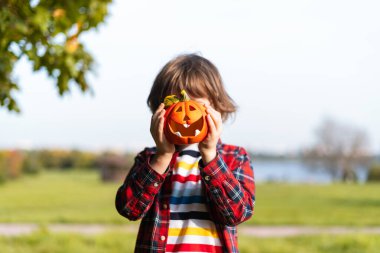 Tatlı çocuk Cadılar Bayramı 'nda sonbahar parkında balkabağıyla oynuyor. Çocuklar şeker mi şaka mı? Sonbaharda eğlence. Giyinik çocuk..