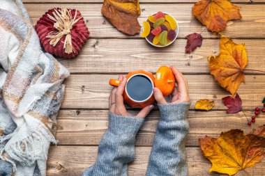Kadın eli gri süveter, balkabağı stili kahve ve sonbahar temalı süslemeler, düşmüş yapraklar ve ahşap arka planda şekerler. Düz yat, boşluğu kopyala