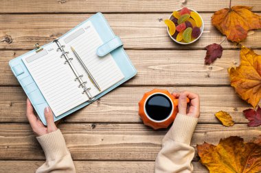 Kadın eli süveter, balkabağı stili kahve ve sonbahar temalı süsleme, düşmüş yapraklar ve ahşap arka planda not defteri olan üst görünüm kompozisyonu. Düz yat, boşluğu kopyala.