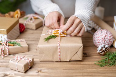 Noel hediyesini paketleyen kadınların elleri, kapatın. Ahşap zemin üzerinde dekoratif öğeler ve malzemelerle hazırlıksız hediyeler, üst görünüm. Noel ya da Yeni Yıl Kutlama Konsepti. Adım adım.