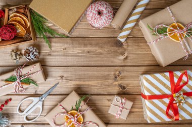 Dümdüz uzanmış Noel hediyesi. Ahşap zemin üzerinde portakal, tarçın, kurdele, makas, ladin dalı, dekor unsurları ve malzemelerle hazırlıksız hediyeler. Yeni yıl DIY paketleme kavramı