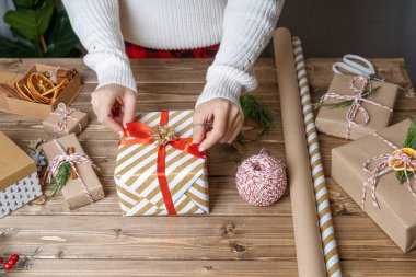 Noel hediyesini paketleyen kadınların elleri, kapatın. Ahşap zemin üzerinde dekoratif öğeler ve malzemelerle hazırlıksız hediyeler, üst görünüm. Noel ya da Yeni Yıl Kutlama Konsepti. Adım adım.