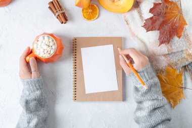 Masaüstü planlayıcısı. Kadın eli süveter, balkabağı, şekerli bir fincan kahve ve sonbahar süslemesi, beyaz arka planda düşmüş yapraklar. Düz yat, boşluğu kopyala