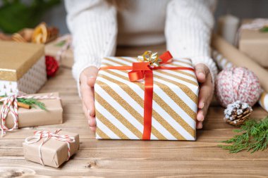 Noel hediyesini paketleyen kadınların elleri, kapatın. Ahşap zemin üzerinde dekoratif öğeler ve malzemelerle hazırlıksız hediyeler, üst görünüm. Noel ya da Yeni Yıl Kutlama Konsepti. Adım adım.