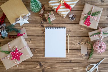 Masaüstü planlayıcısı. Açık bir defter ve Noel hediyesi paketleri. Dekor unsurlarıyla ahşap arka planda sunumlar, üst görünüm. Yeni yıl paketleme kavramı, üst görünüm