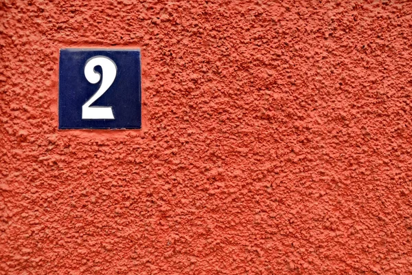 Number 2 / two, blue and white digit on burgundy red surface.