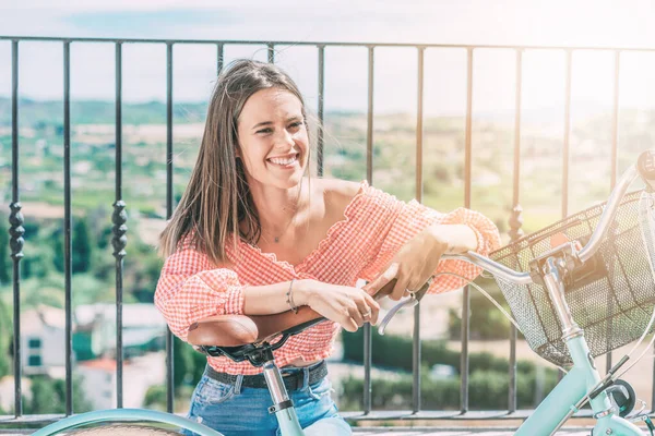 Young smiling woman with bicycle, rests sitting with beautiful landscape in the background