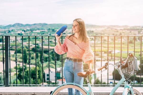 Young woman with a bicycle, resting and drinking from a bottle