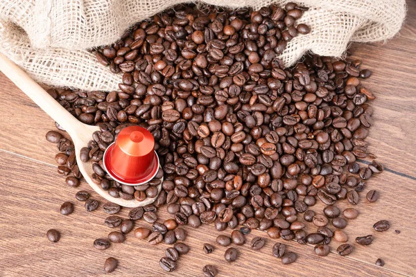 Coffee capsule on wooden spoon and  roasted coffee beans with burlap sack on wooden background.top view.