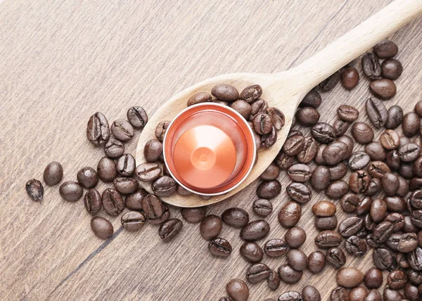 Coffee capsule on wooden spoon and  roasted coffee beans  on wooden background,top view,close up.