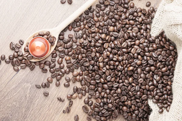 Coffee capsule on wooden spoon and  roasted coffee beans with burlap sack on wooden background,top view.