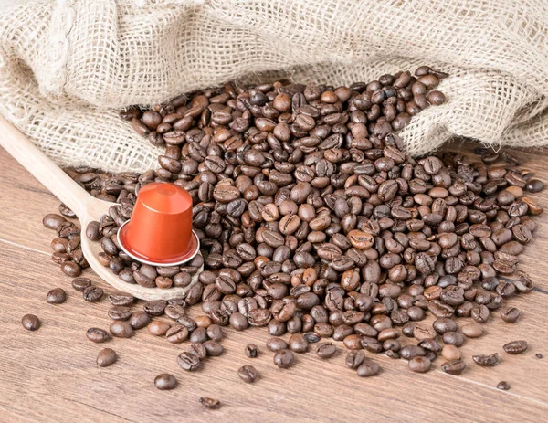 Coffee capsule on wooden spoon and  roasted coffee beans with burlap sack on wooden background.