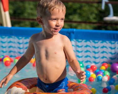 Sıcak yaz gününde renkli şişme halka açık yüzme havuzunda oynamaktan mutlu çocuk çocuk. Yüzmeyi öğrenmek. Çocuk su oyuncakları.