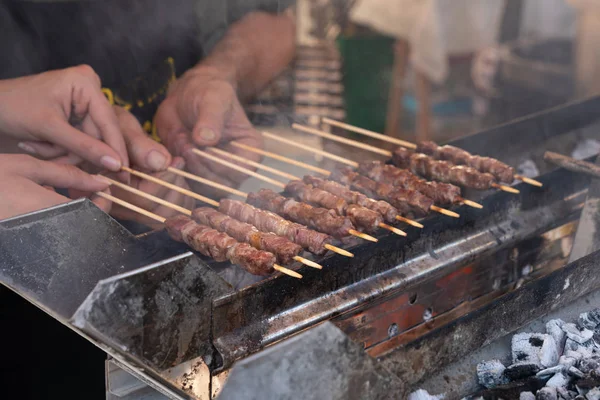 Man cooking marinated meat on wooden skewer