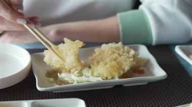 Elinde çubuk olan bir kadın ince dilimlenmiş Japon sebze tempurası ve zencefilli ponzu soslu sağlıklı vejetaryen yemeği alır. Restoran masasında servis edilen lezzetli Asya yemeği.