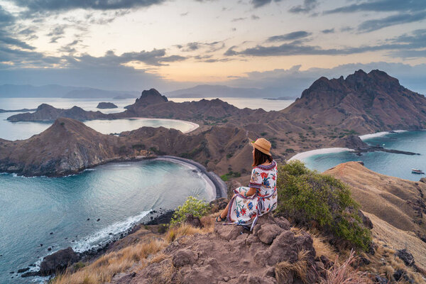 Young woman traveller sitting and relaxing on top of Padar island at evening sunset, Komodo national park in Indonesia, Asia