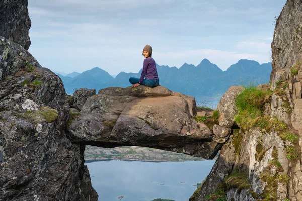 Genç mutlu Asyalı kadın Djevelporten 'de oturuyor ya da Floya dağ yolunda Şeytan' ın Kapısı 'nda. Gülen suratlı bir kadın. Lofoten adasındaki balıkçı köyü, İskandinavya, Avrupa