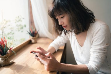 Akıllı telefon kullanıp video izleyip online oyun oynayan Asyalı genç bir kadın. Teknoloji sektörü ve sosyal uzaklık kavramı. Bangkok, Tayland
