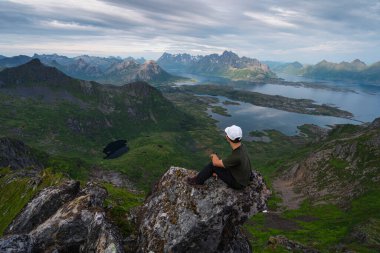 Yaz mevsiminde Kuzey Norveç, İskandinavya, Avrupa 'da, Lofoten Adası' ndaki Floya Dağı 'nın zirvesinde oturan Asyalı genç yürüyüşçü.