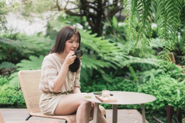 Genç Asyalı kadın bahçede oturup bir fincan kahve içiyor. Doğal yaşam tarzını seven bir kadın. Bangkok, Tayland