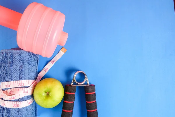 Fitness concept with dumbbell,hand gripper,tower and measuring tape on a blue background.
