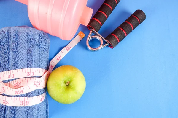 Fitness concept with dumbbell,hand gripper,tower and measuring tape on a blue background.