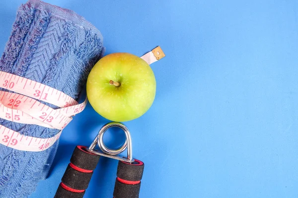 Fitness concept with dumbbell,hand gripper,tower and measuring tape on a blue background.