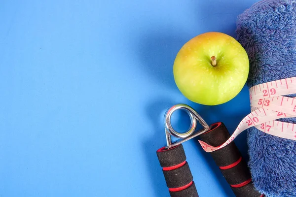 Fitness concept with dumbbell,hand gripper,tower and measuring tape on a blue background.