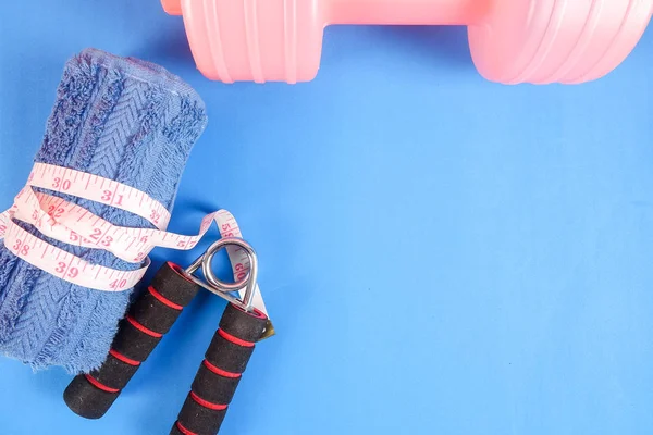 Fitness concept with dumbbell,hand gripper,tower and measuring tape on a blue background.