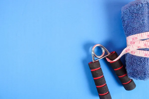 Fitness concept with dumbbell,hand gripper,tower and measuring tape on a blue background.