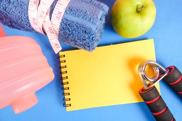 Fitness concept with dumbbell,hand gripper,tower and measuring tape on a blue background.