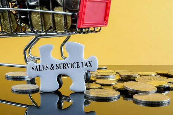 SALES & SERVICE TAX conceptual text. Trolley,coins and jigsaw puzzle with reflection on a yellow background. Sales and shopping concept
