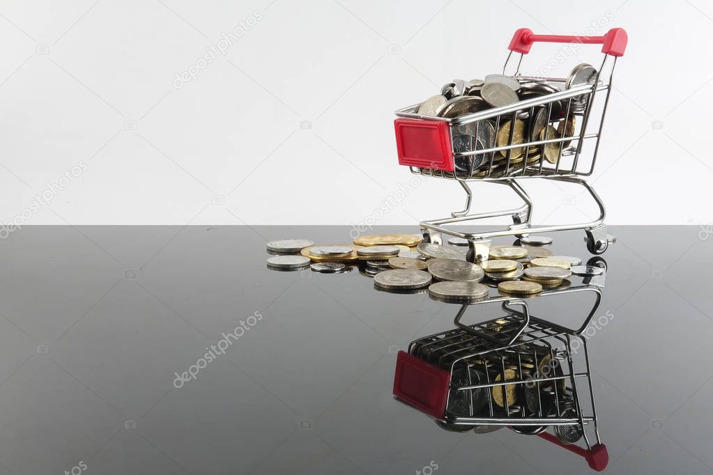 Trolley and coins isolated on white with reflection. Sales and shopping concept